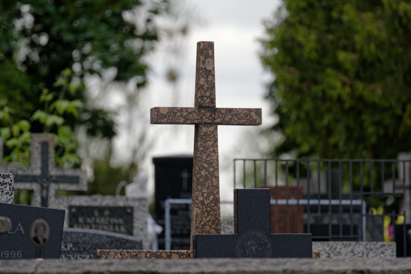 A granite grave cross standing in a peaceful cemetery setting